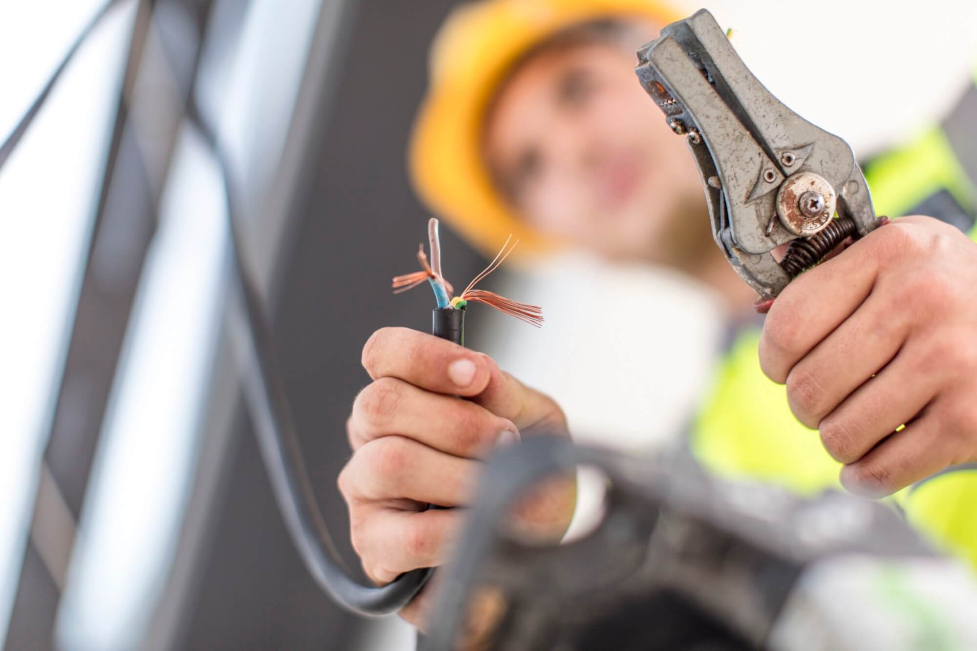 En elektriker med gul hjälm använder en kabelskalare för att strippa en elkabel under installation.